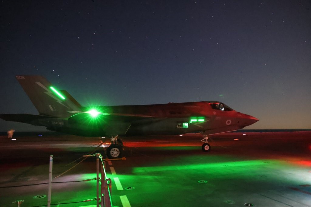 F-35B Lightning on runway at night, lit by green lights.